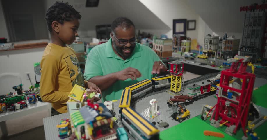 Man and a child interacting with a moving toy train on a playset