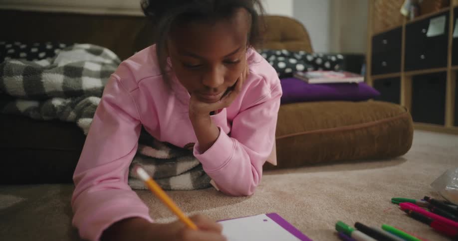 A girl lays down on the living room floor doing homework