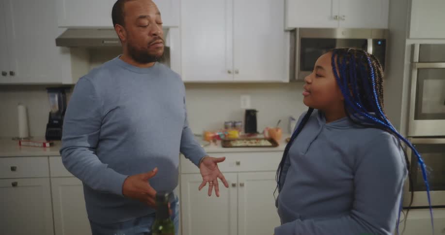 A father talking to his daughter with braided blue hair in their kitchen at home