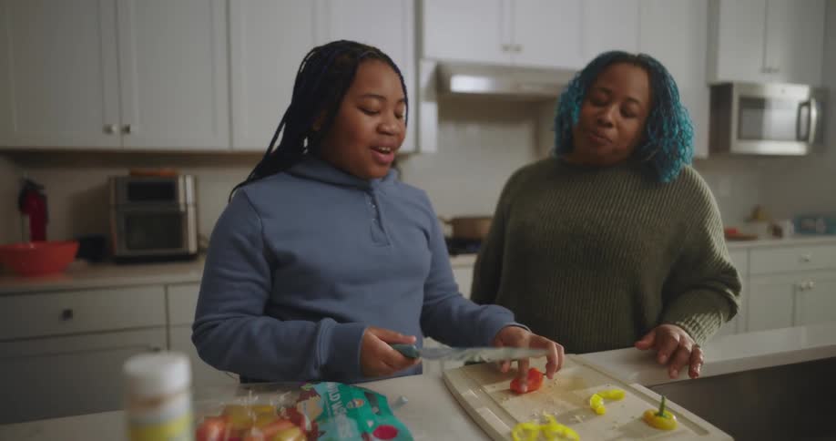 A teenager is cutting peppers in the kitchen