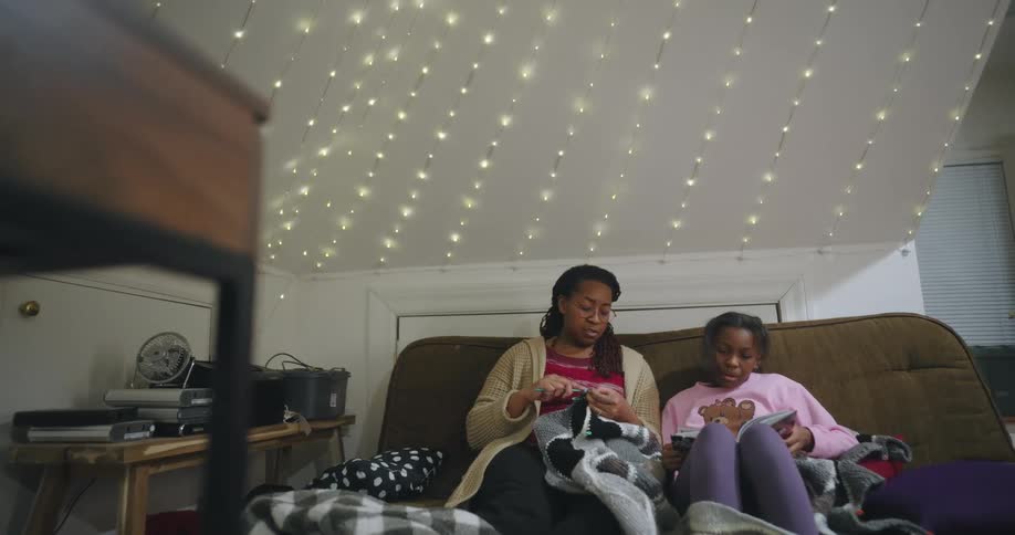 Mother crochets while sitting next to her daughter and listening to the girl read
