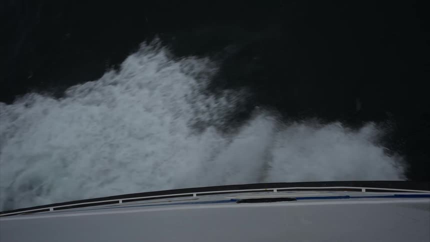 From a topdown viewpoint the bow of a ship slices through dark water producing a surge of white foam along its hull while the oceans deep surface extends outward in stark contrast to the vessels movement