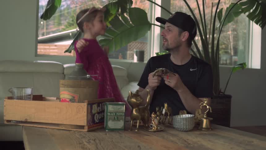 A father shows his daughter wearing a cat ears tiara and a dress a collection of antique decorations