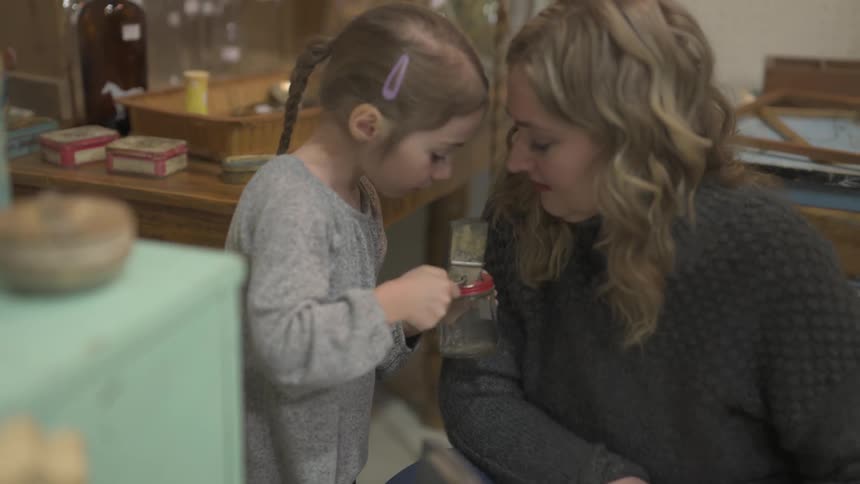 A girl winds a gadget on a jar as her mother watches