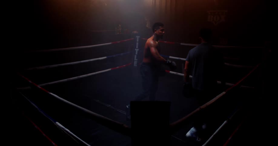 Two men are boxing together in a dark lit room