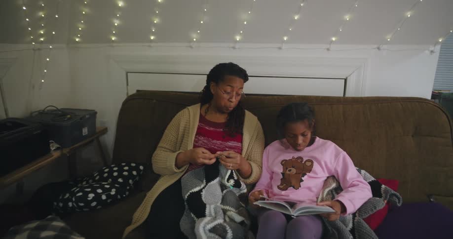 Mother sits on a couch crocheting while listening to her daughter read