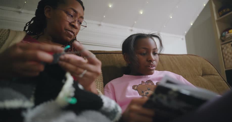 Mother sitting in the living room crochets while listening to her daughter read