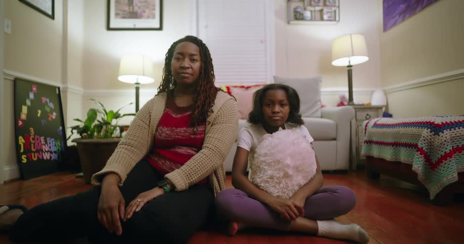 A mother and daughter sit together on the floor of a modern living room