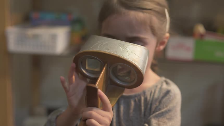 An adult helps a child to use a vintage stereoscope viewer