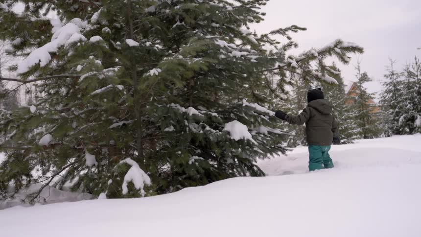 A girl is wading through the snow by the tree