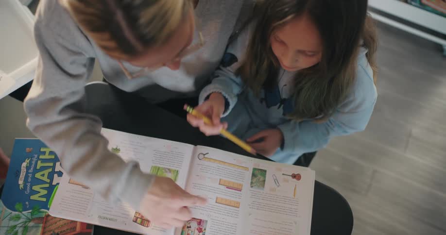A mother reads a schoolbook with her daughter at home