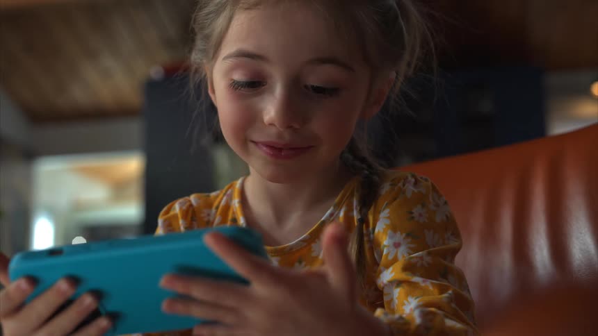 A girl sits on a couch at home playing with a smartphone
