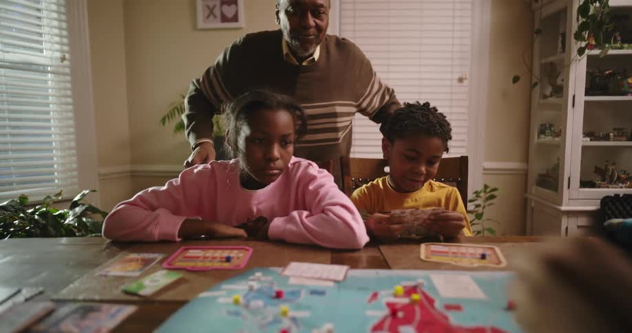 Grandfather standing with his two grandsons playing board game on a wooden table