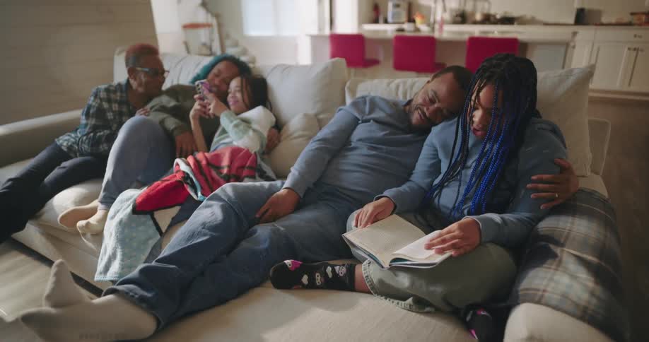 Family sitting and lying on the sofa in the living room reading the book and interacting with smartphone