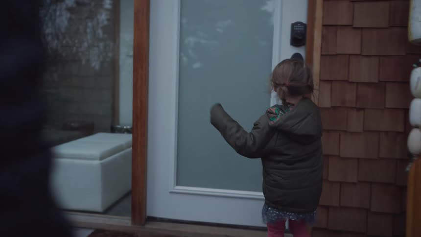 Parent follows their daughter while the girl walks to the front door and grasps the handle on cold day