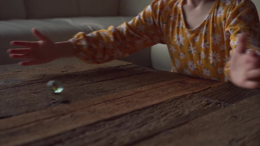Little girl playing with a marble on a wooden table