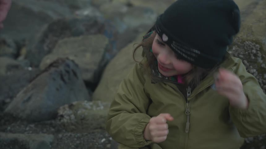 Little girl sitting among rocks listening to the sound of a shell