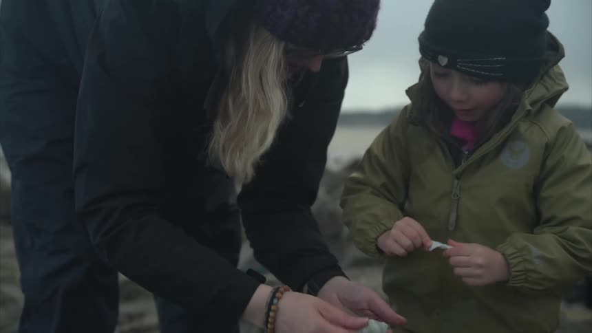 Mother and young son collecting sea shells and placing on large rock
