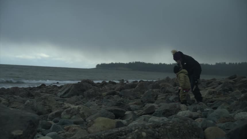 A child digs through the rocks on the shore