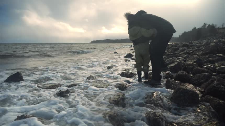 Mother carrying son on rocky shoreline as tide rolls in