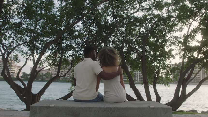 Couple sitting on stone bench front of large tree overlooking the river