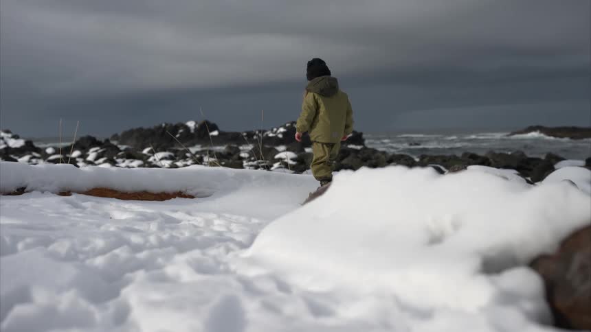 A girl walks over the snow covered rocks