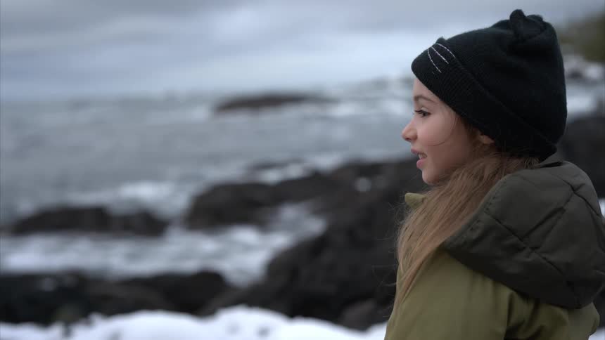 A little girl smiles as she looks at the waves on a rocky beach