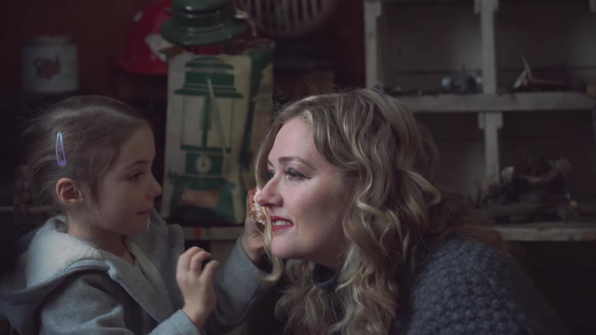 A girl puts a conch she found over the counter of a general store over her mother ear