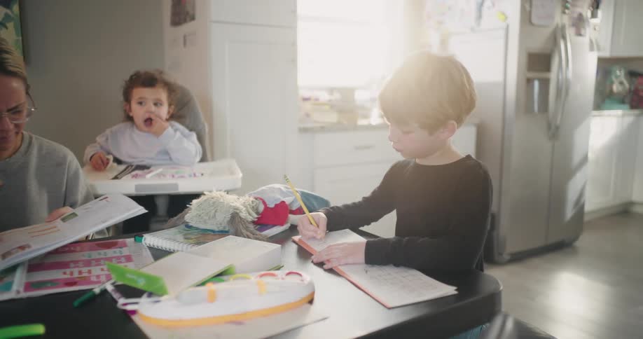 Mother sitting at the table with her four children around her studying and playing