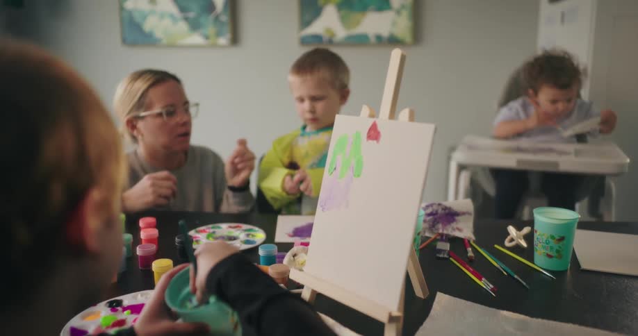 A mother is watching her children paint with water colors
