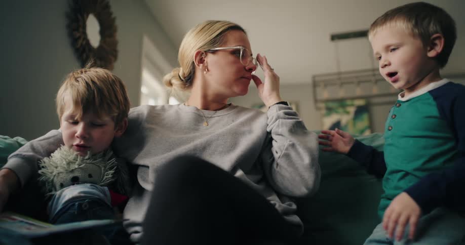 Woman sitting in her living room talks to her younger son while her other son reads a book