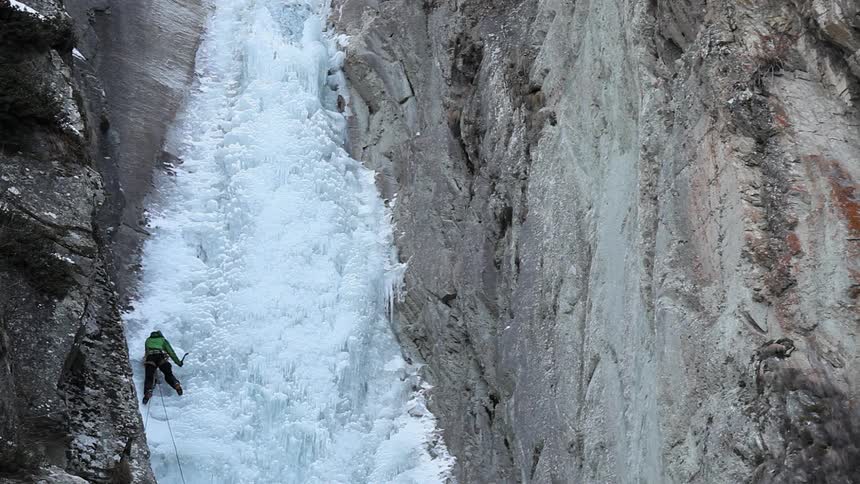 A person is climbing up a frozen waterfall between two cliffs