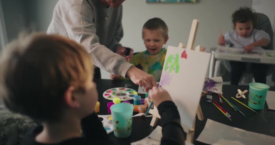 Woman caring for three small children who are interacting with paint on the table