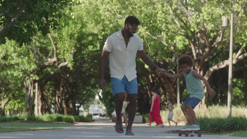 Father teaches his son to ride the skateboard in the park on a sunny day