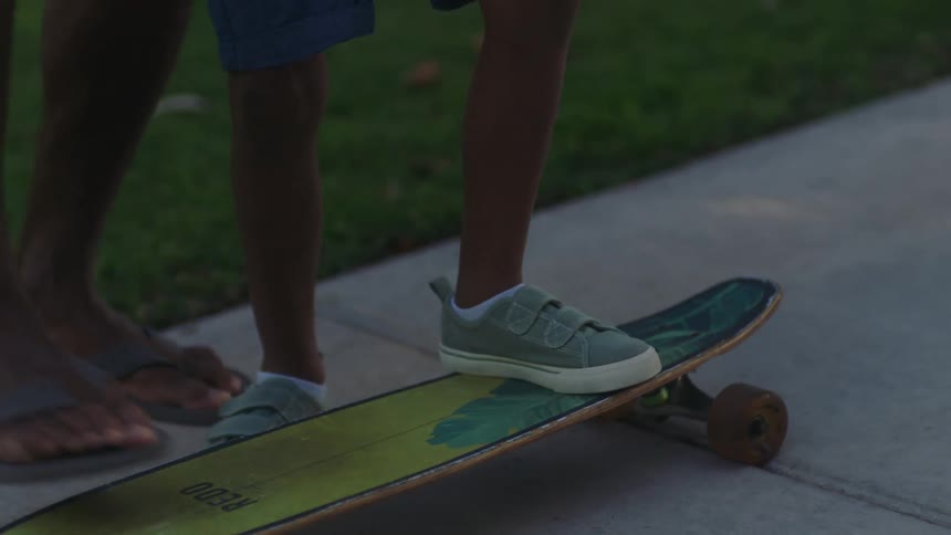 Father teaching his son how to skateboard by positioning his body on top of the platform