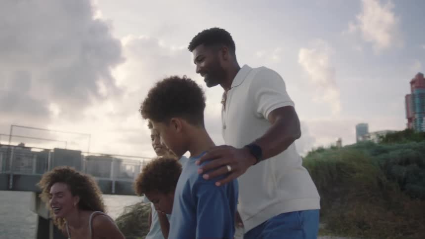A happy family sitting on the coast of a beach near a waterfront city at dusk