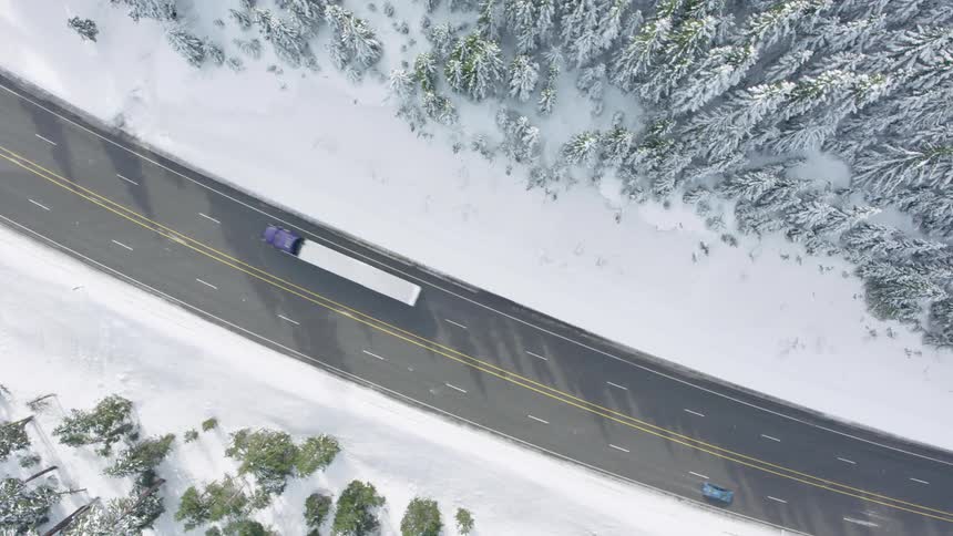 Straight down view of a semi truck and car passing each other on a mountain pass highway