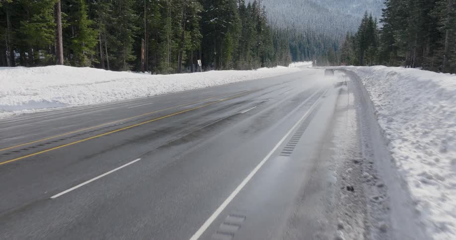 Low push towards a SUV driving on a mountain highway surrounded by deep snow and dense forest