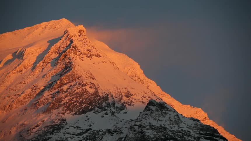 Sunlight shining an orange hue on snow covered mountain at sunset