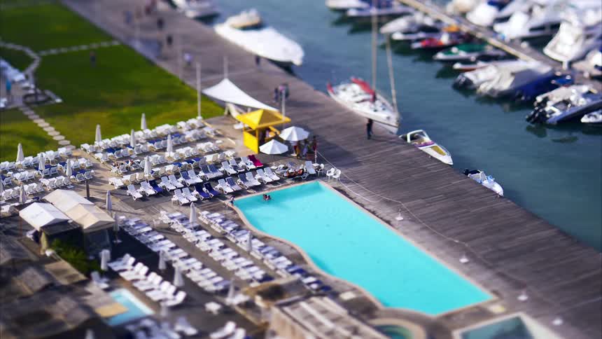 People walk on a boardwalk that have docked boats and a swimming pool