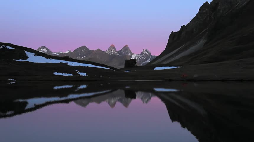 A lake reflects the surrounding mountains and blue sky at dusk