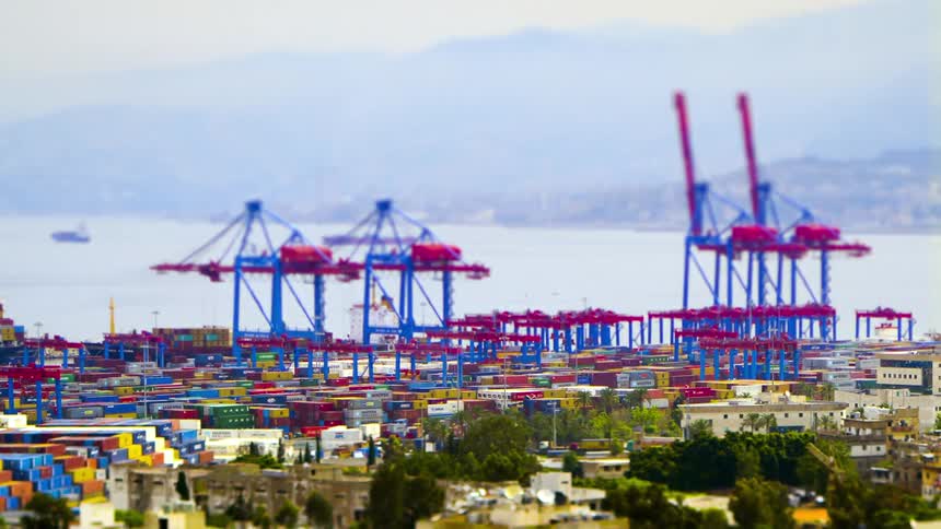 In a bustling shipping port multiple vehicles haul cargo containers past neatly stacked rows while towering cranes unload freight all rendered in a tiltshift effect that lends a miniaturelike quality under a distant coastal backdrop