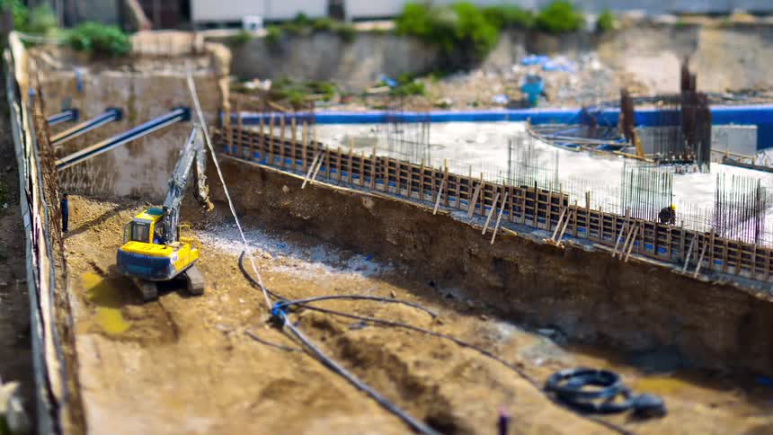 A construction site shows a digger workers and the framework of a structure