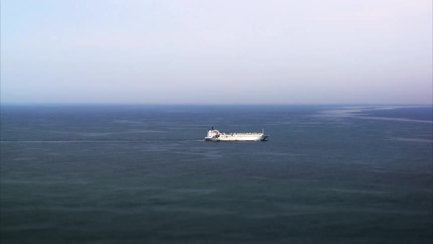 A solitary cargo ship sails across a vast dark blue ocean under a pale sky