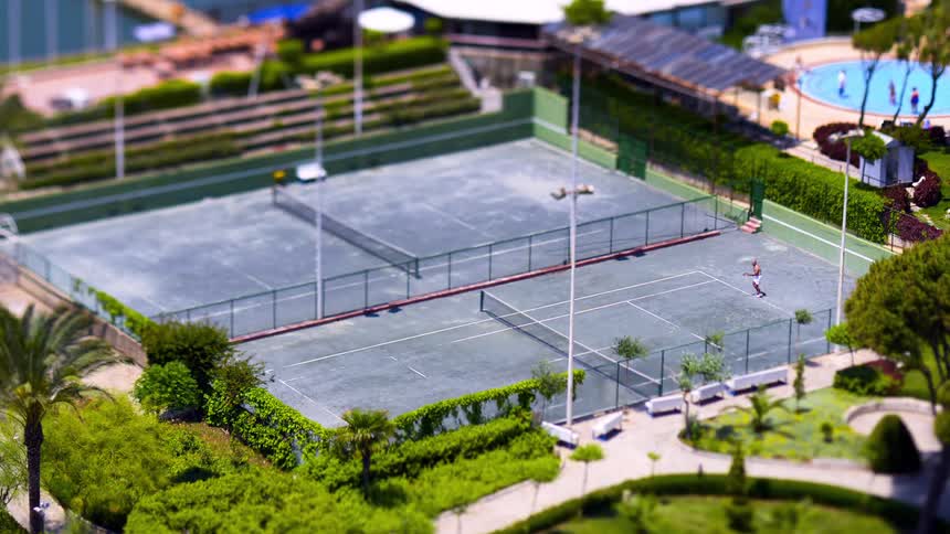 People play tennis on a court near a swimming pool on a sunny summer day