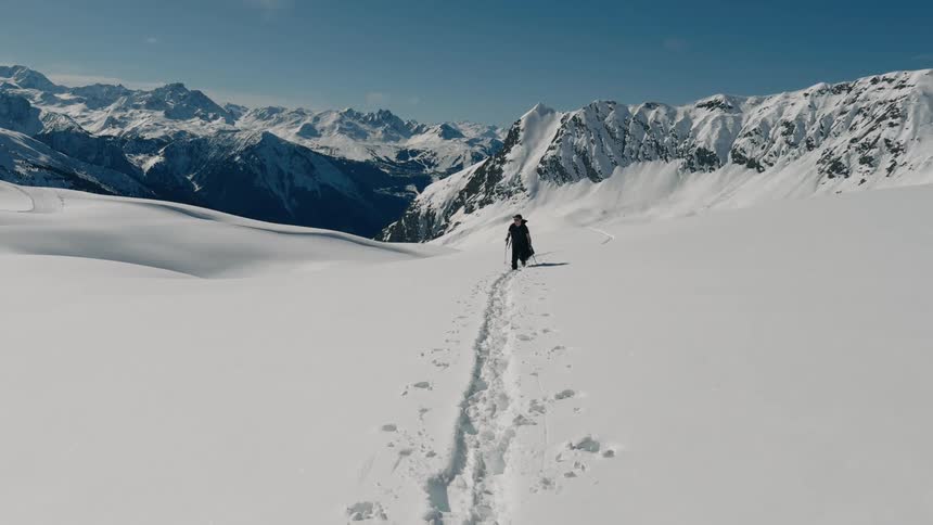 A person hikes through the snow in front of snowcovered mountains