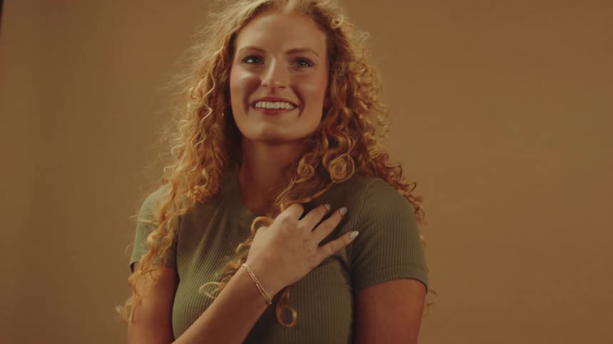 Woman is smiling and touching her hair while she does a pose