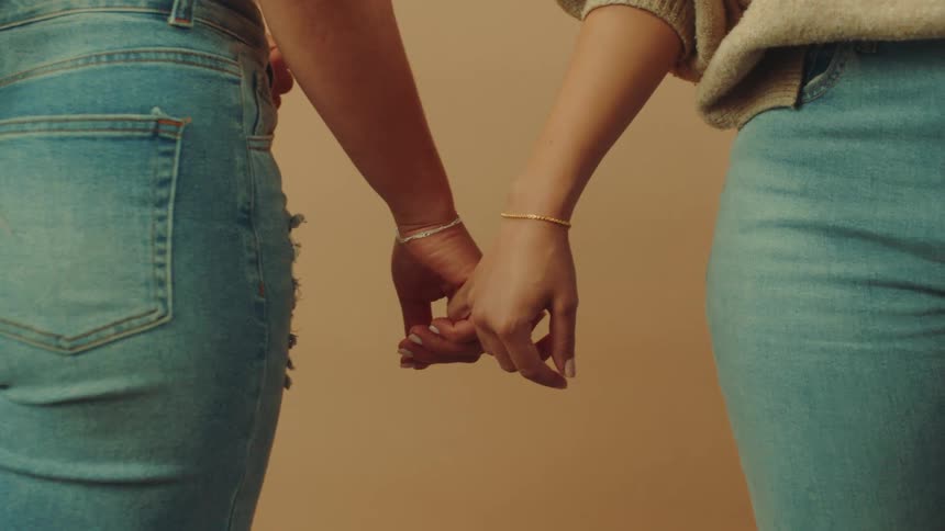 Two females stand together holding hands by their pinky fingers