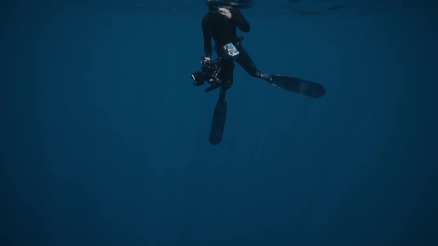 Scuba diver is under the ocean water with a video camera