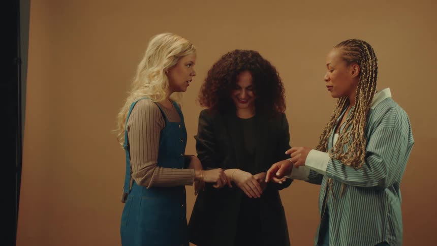 Three women and a foot standing next to each other showing their wrists with jeweled bracelets